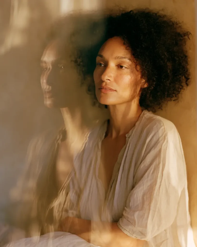 Woman reflected in glass in soft morning light, symbolising identity transformation during matrescence.